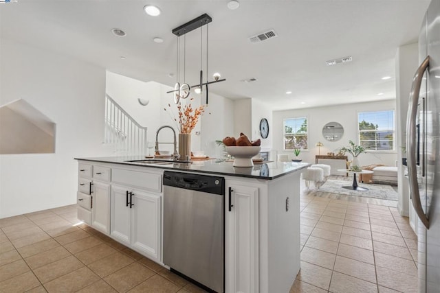 kitchen with decorative light fixtures, stainless steel appliances, a center island with sink, white cabinetry, and sink