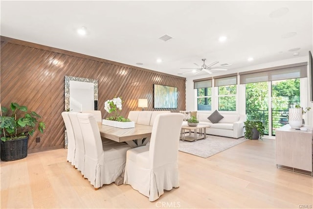 dining room with ceiling fan, light wood-type flooring, and wooden walls