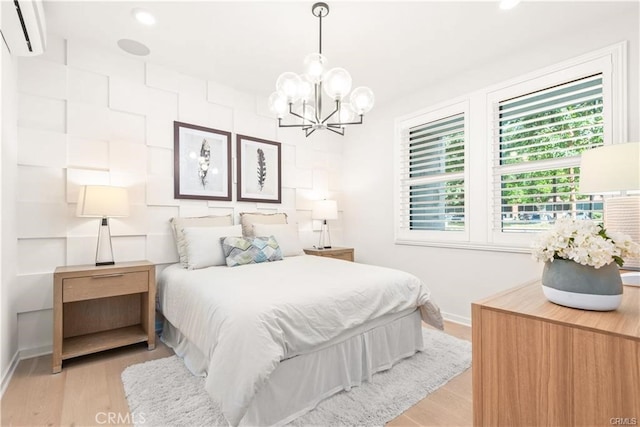 bedroom featuring light wood-type flooring, a wall unit AC, and a notable chandelier