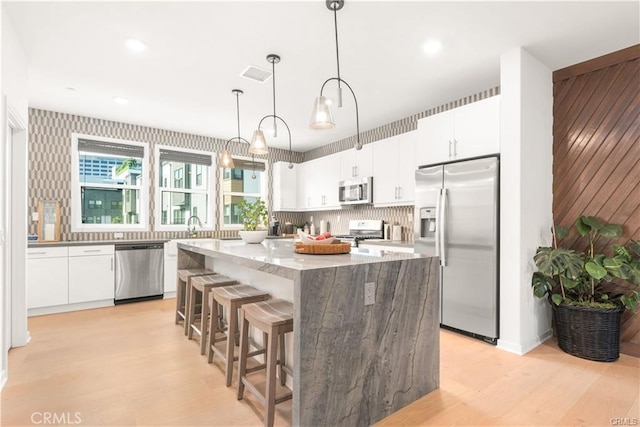 kitchen with a kitchen island, white cabinets, hanging light fixtures, and appliances with stainless steel finishes