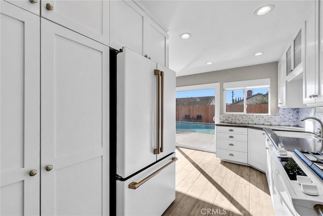 kitchen featuring white appliances, white cabinetry, light hardwood / wood-style floors, sink, and backsplash