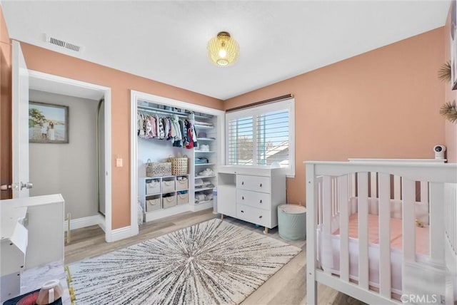 bedroom with a closet, a crib, and light hardwood / wood-style flooring