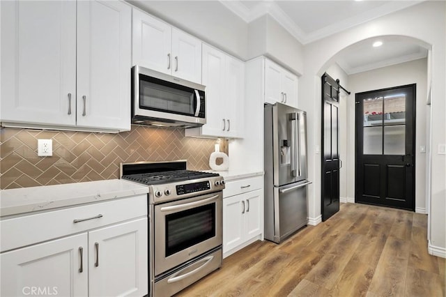 kitchen featuring white cabinets, a barn door, appliances with stainless steel finishes, and tasteful backsplash