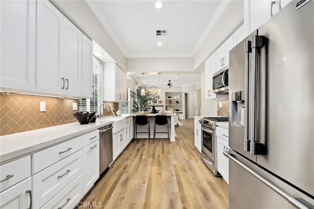 kitchen with white cabinets, stainless steel appliances, decorative backsplash, sink, and light hardwood / wood-style floors