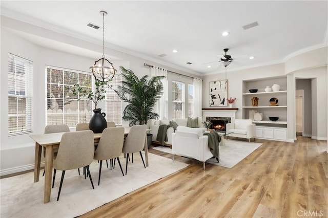 dining space featuring light wood-type flooring, plenty of natural light, a premium fireplace, and ornamental molding