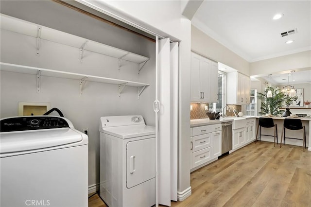 laundry room featuring sink, a notable chandelier, washer and dryer, and light hardwood / wood-style flooring