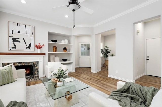 living room with ceiling fan, a fireplace, light hardwood / wood-style flooring, built in features, and ornamental molding