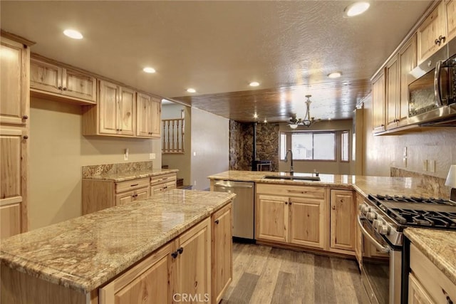 kitchen featuring light hardwood / wood-style floors, stainless steel appliances, a center island, sink, and an inviting chandelier