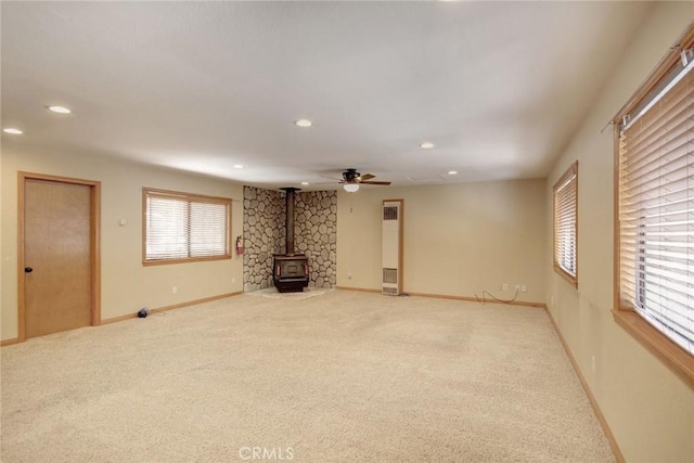 interior space with ceiling fan, a wood stove, and light colored carpet