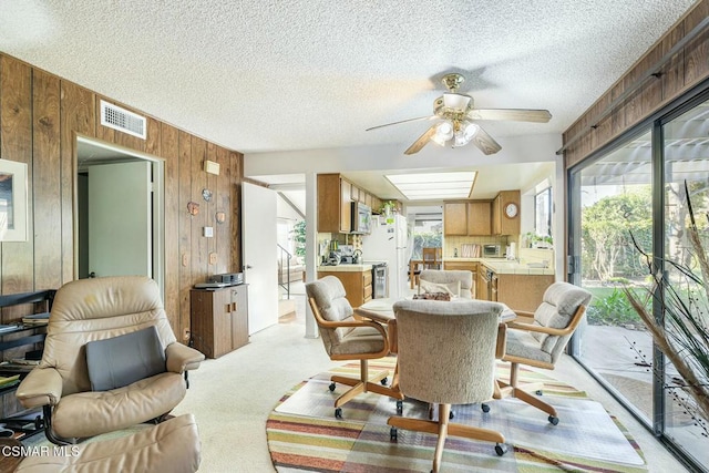 carpeted dining room with wooden walls, a textured ceiling, and ceiling fan