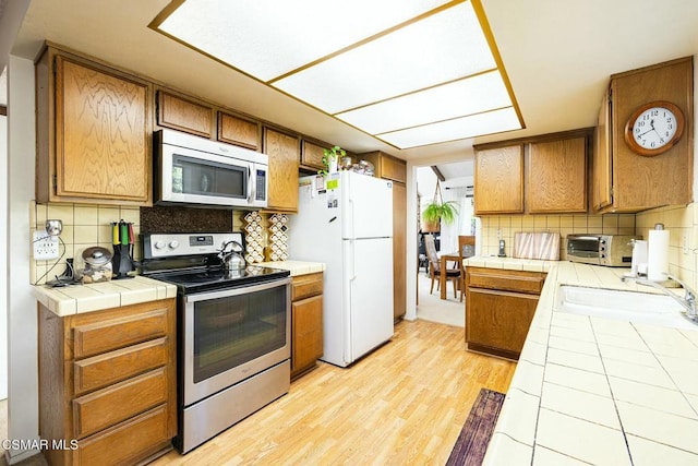 kitchen featuring tile countertops, light hardwood / wood-style flooring, stainless steel appliances, backsplash, and sink