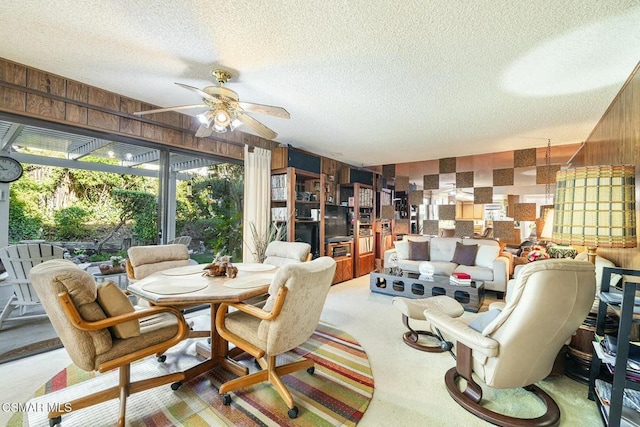 dining space featuring a textured ceiling, wood walls, ceiling fan, and carpet flooring