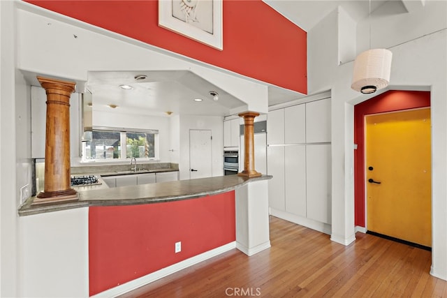 kitchen with ornate columns, light hardwood / wood-style floors, pendant lighting, white cabinets, and sink