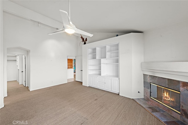 carpeted living room featuring lofted ceiling, built in shelves, a tiled fireplace, and ceiling fan