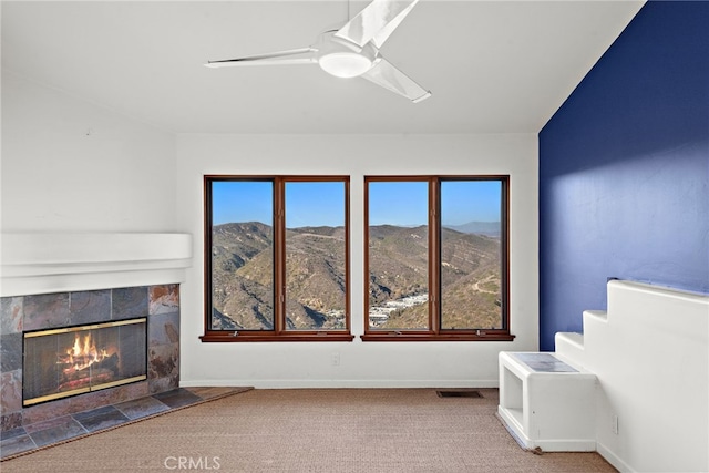 living room with a tile fireplace, light carpet, ceiling fan, and a mountain view