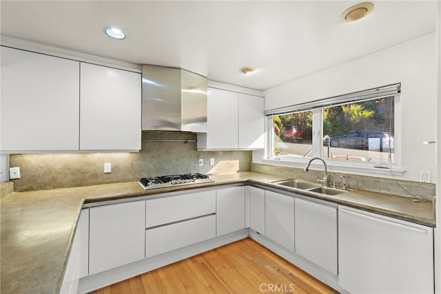 kitchen with wall chimney range hood, stainless steel gas cooktop, backsplash, white cabinetry, and sink