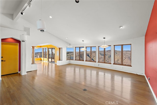 unfurnished living room with track lighting, wood-type flooring, a mountain view, and vaulted ceiling with beams