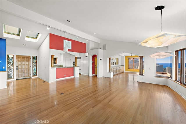 unfurnished living room with light wood-type flooring, high vaulted ceiling, track lighting, and a skylight