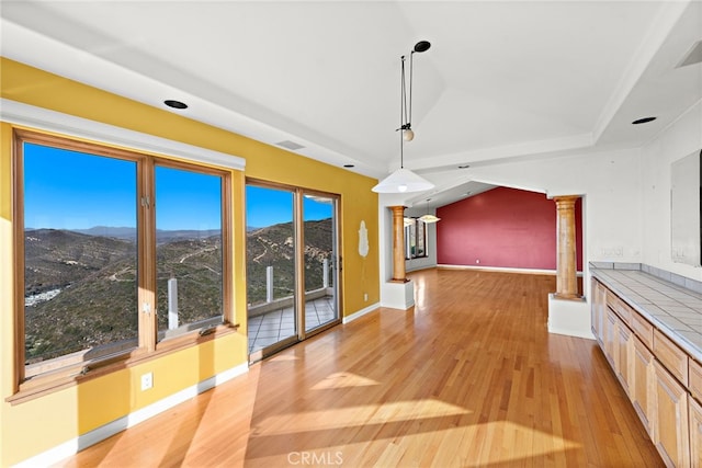 unfurnished dining area featuring light wood-type flooring, decorative columns, and a mountain view