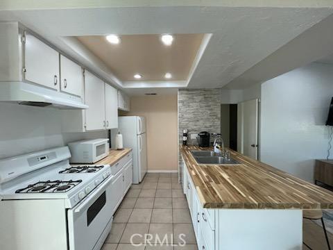 kitchen with white appliances, white cabinets, sink, a raised ceiling, and light tile patterned flooring