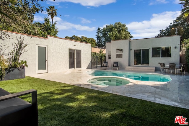 rear view of property featuring a swimming pool with hot tub, a patio area, and a lawn