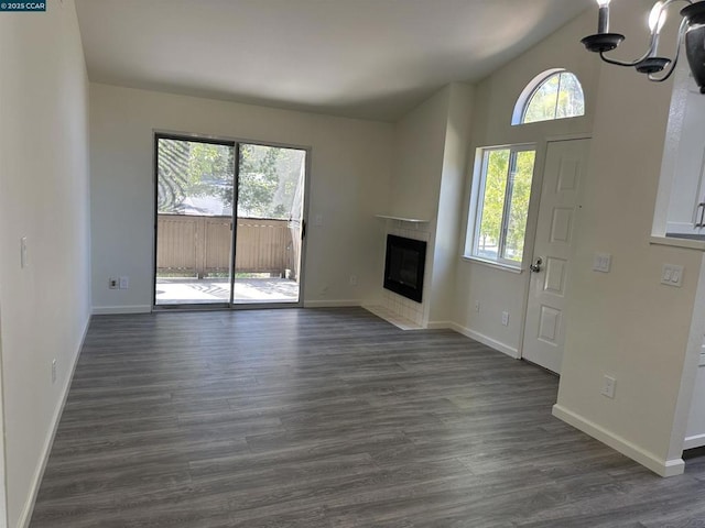 unfurnished living room featuring lofted ceiling, a fireplace, a chandelier, and dark hardwood / wood-style floors