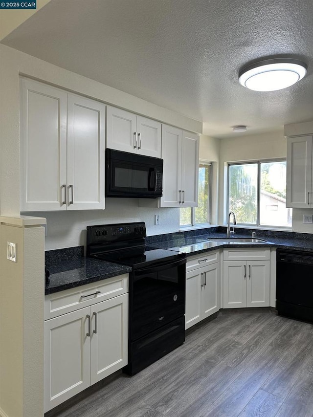 kitchen featuring a textured ceiling, black appliances, hardwood / wood-style floors, white cabinetry, and sink