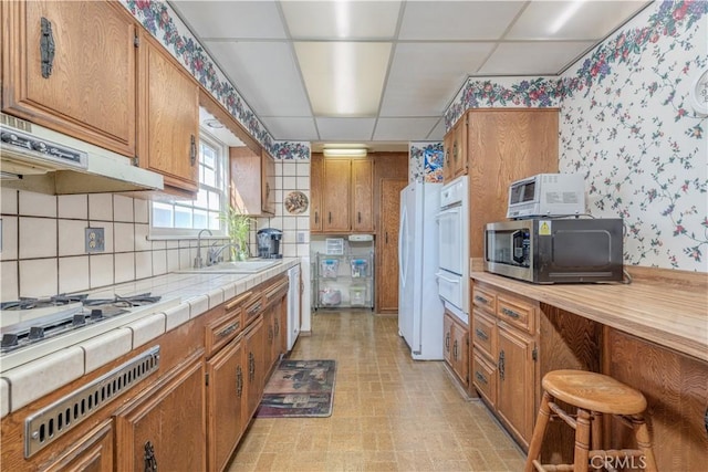 kitchen with white appliances, tile counters, a drop ceiling, tasteful backsplash, and sink