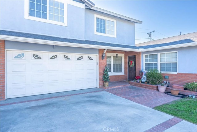 traditional-style home featuring driveway, brick siding, a shingled roof, an attached garage, and stucco siding