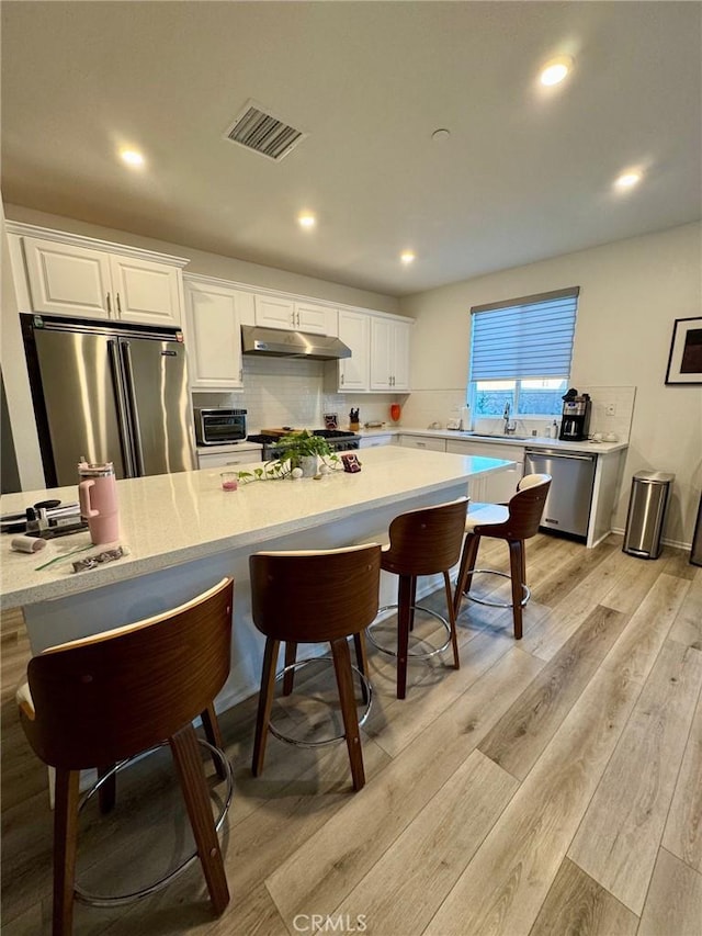 kitchen featuring light hardwood / wood-style flooring, stainless steel appliances, a spacious island, tasteful backsplash, and white cabinetry