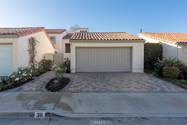 mediterranean / spanish-style home featuring driveway, a tiled roof, a gate, and stucco siding