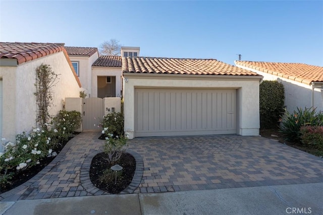 mediterranean / spanish home with stucco siding, a gate, decorative driveway, and a tiled roof