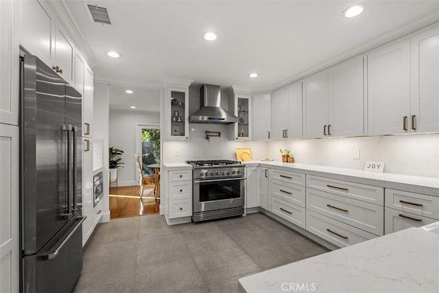 kitchen featuring premium appliances, visible vents, white cabinets, wall chimney exhaust hood, and glass insert cabinets