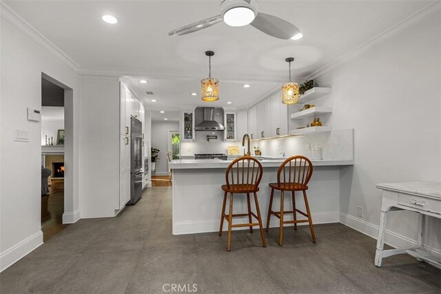 kitchen featuring a breakfast bar area, kitchen peninsula, ceiling fan, white cabinets, and wall chimney range hood