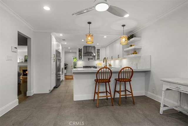 kitchen with a peninsula, white cabinets, wall chimney exhaust hood, glass insert cabinets, and crown molding