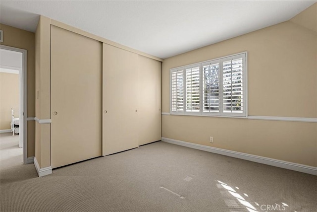 unfurnished bedroom with vaulted ceiling, a closet, and light carpet