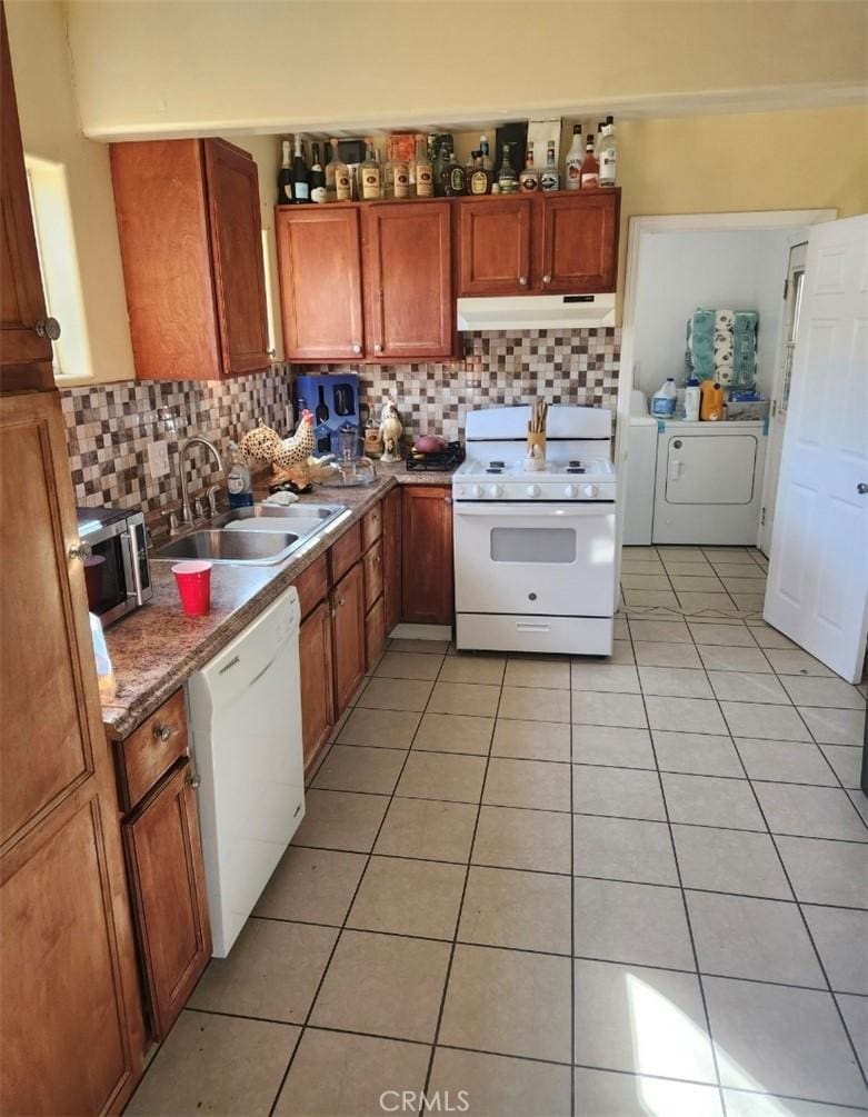 kitchen featuring brown cabinetry, a sink, washer and dryer, white appliances, and under cabinet range hood