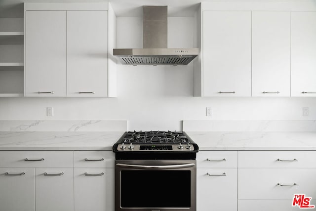 kitchen with light stone counters, white cabinets, stainless steel gas stove, and wall chimney range hood