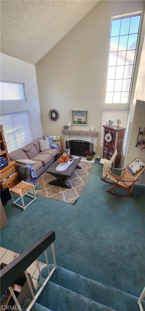 carpeted living room featuring high vaulted ceiling, a fireplace, and a textured ceiling