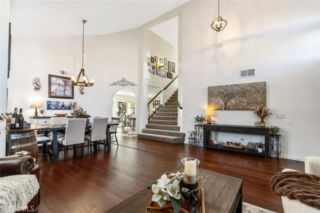 living area featuring arched walkways, visible vents, dark wood-type flooring, stairs, and a chandelier