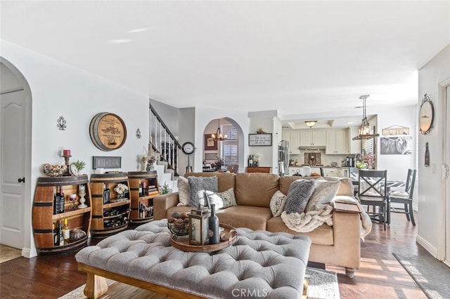 living area with arched walkways, a notable chandelier, dark wood-type flooring, baseboards, and stairs