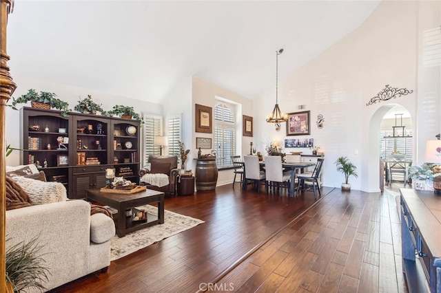 living area with high vaulted ceiling, arched walkways, a notable chandelier, and dark wood finished floors