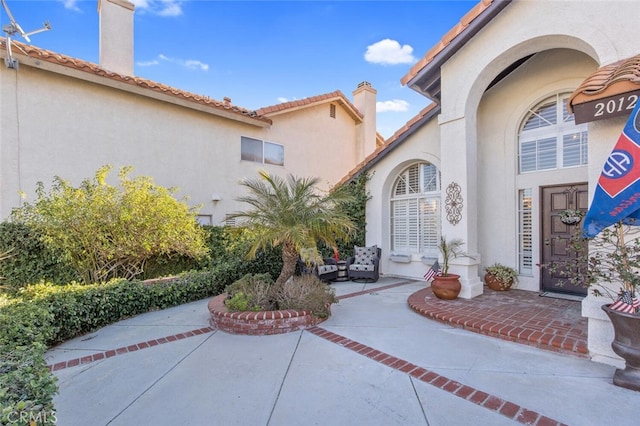 doorway to property featuring a patio, a chimney, and stucco siding