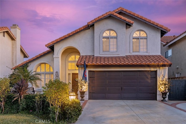 mediterranean / spanish-style house featuring concrete driveway, a tiled roof, an attached garage, and stucco siding