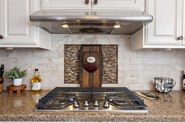 kitchen featuring under cabinet range hood, stainless steel gas stovetop, white cabinets, and decorative backsplash