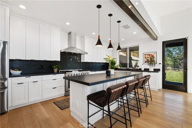 kitchen with a breakfast bar area, stainless steel appliances, a kitchen island, white cabinets, and wall chimney range hood