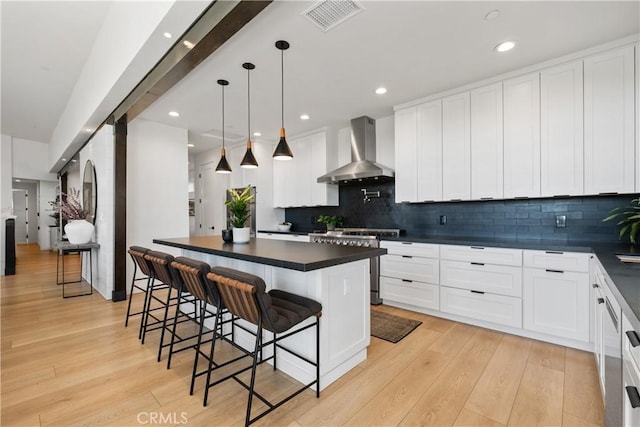 kitchen with a kitchen breakfast bar, hanging light fixtures, white cabinetry, wall chimney range hood, and high end stainless steel range