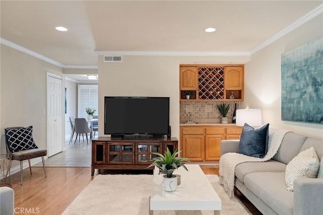 living room featuring indoor bar, light hardwood / wood-style flooring, and crown molding