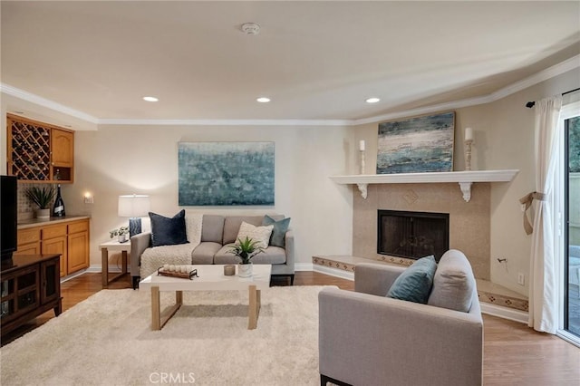 living room with a high end fireplace, ornamental molding, and light hardwood / wood-style floors