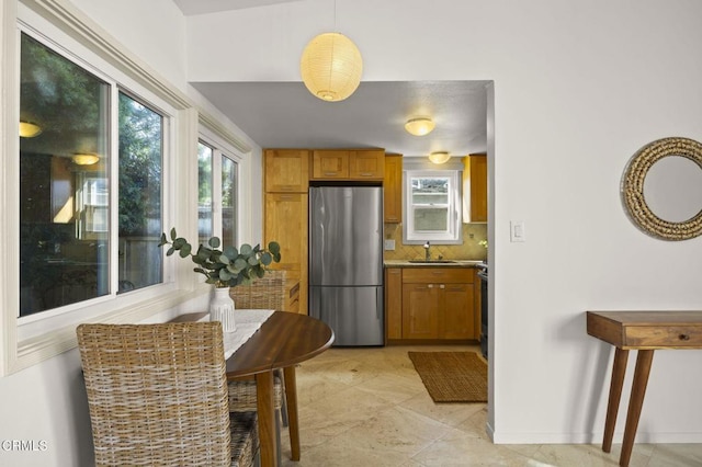 kitchen featuring stainless steel refrigerator, hanging light fixtures, decorative backsplash, and sink